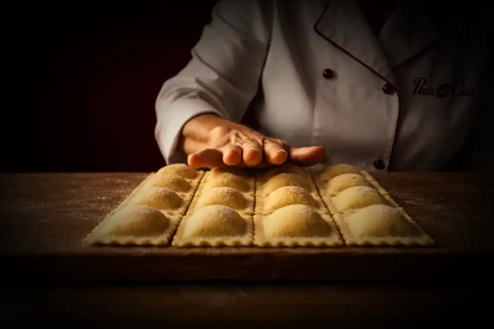 Las manos del chef acomodando raviolis recién cortados sobre la tabla enharinada